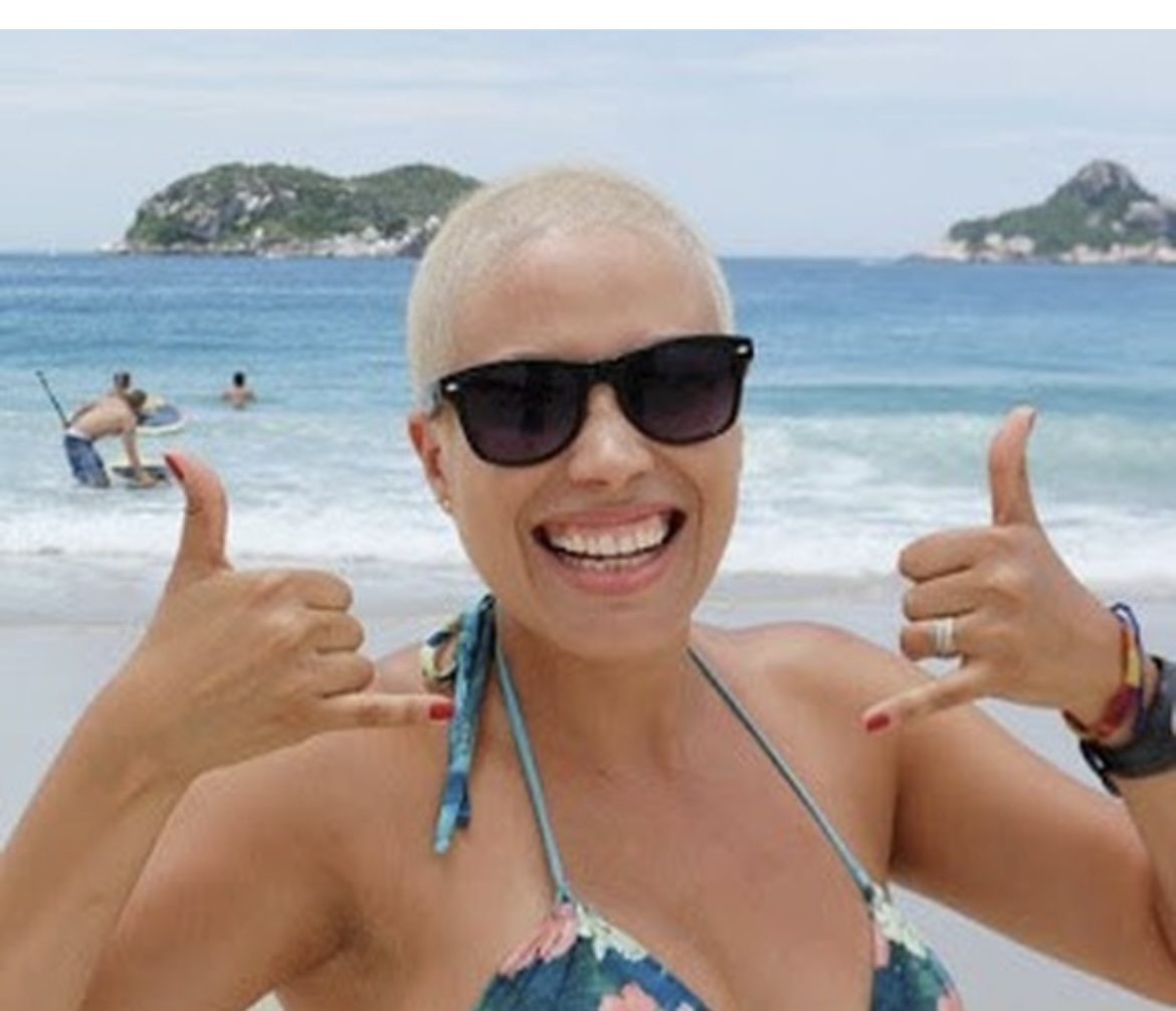 Patrícia na praia, sorrindo, com os polegares para cima